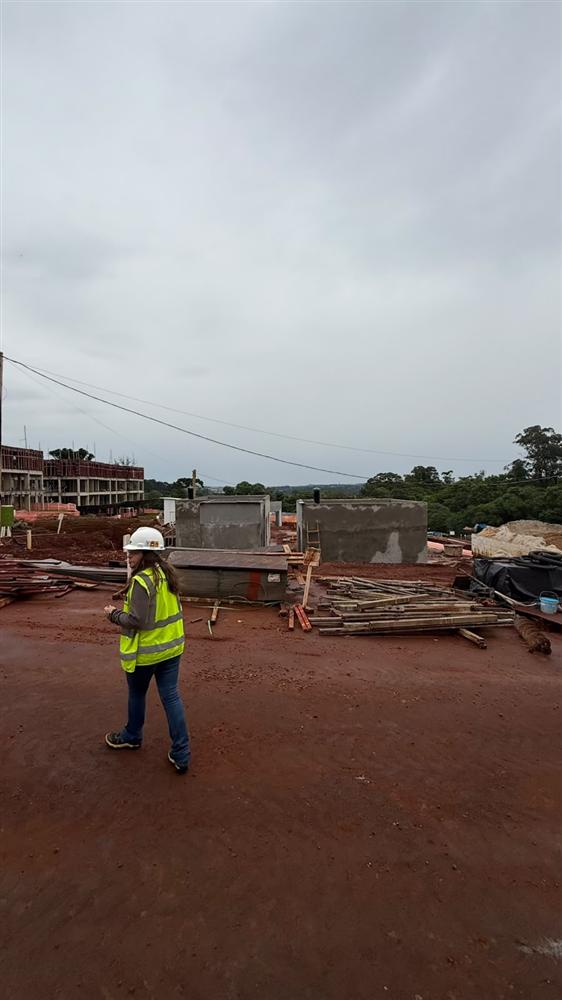 Profissional de colete e capacete caminhando pelo canteiro de obras